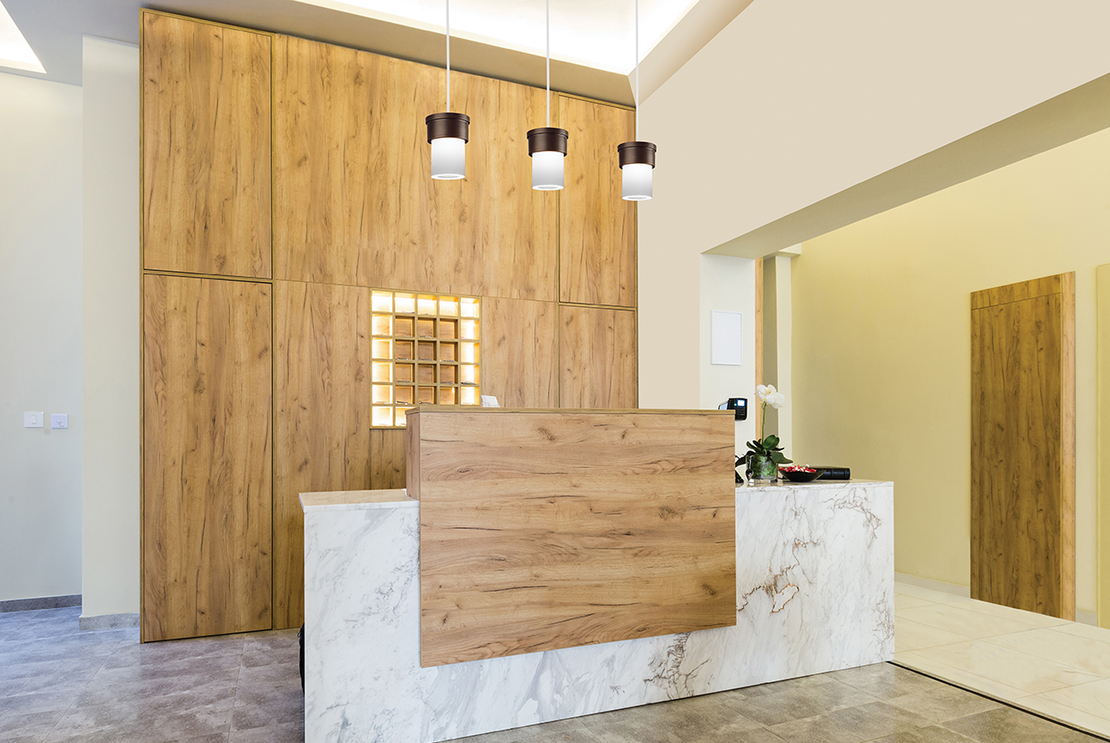A small, luminous cylinder pendant with a solid base shown in a hotel lobby above the reception desk
