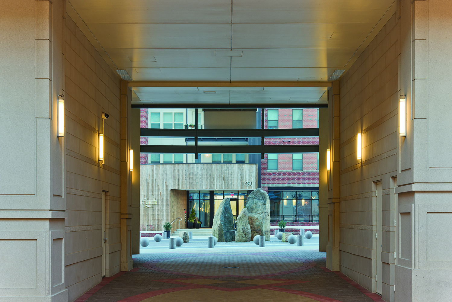 Raven outdoor light fixtures along an exterior passageway between buildings in an outdoor commercial area.