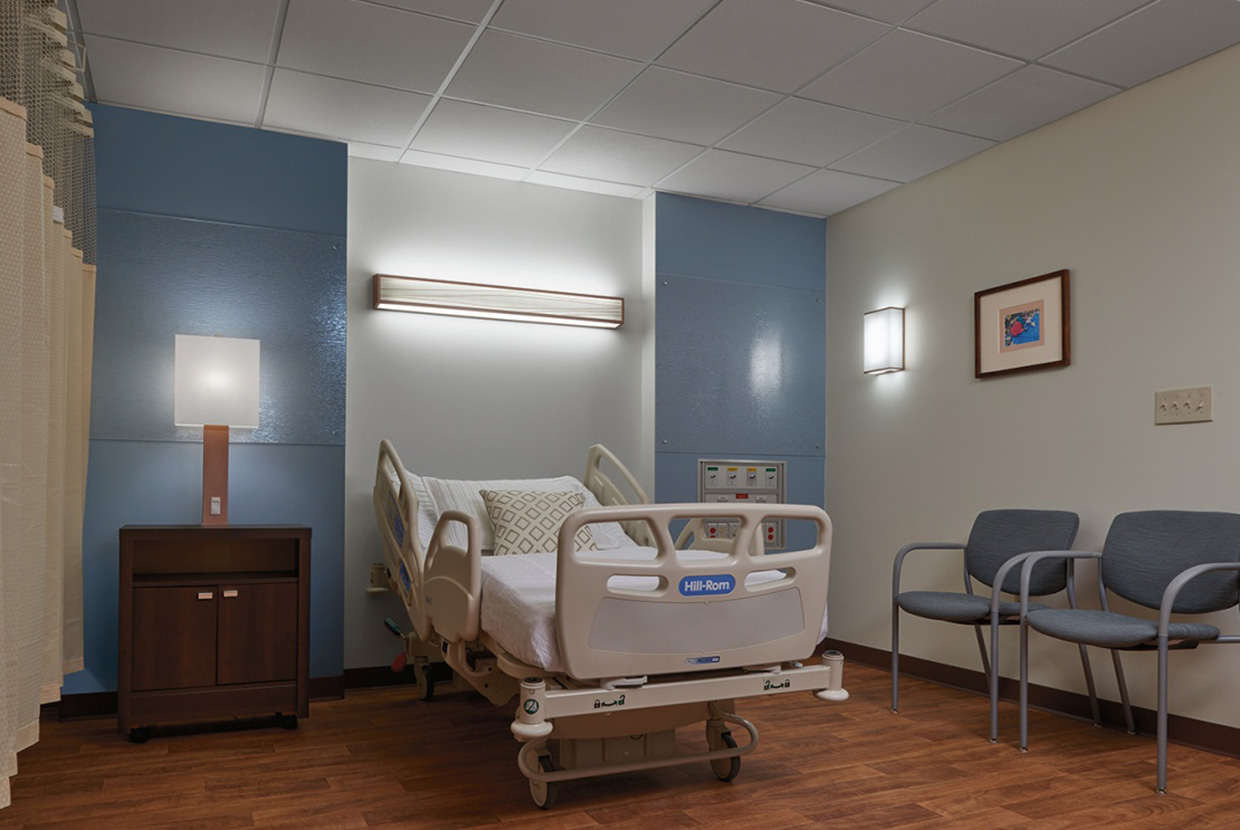 Hospital patient room with headwall, table lamp, and wall sconce. 