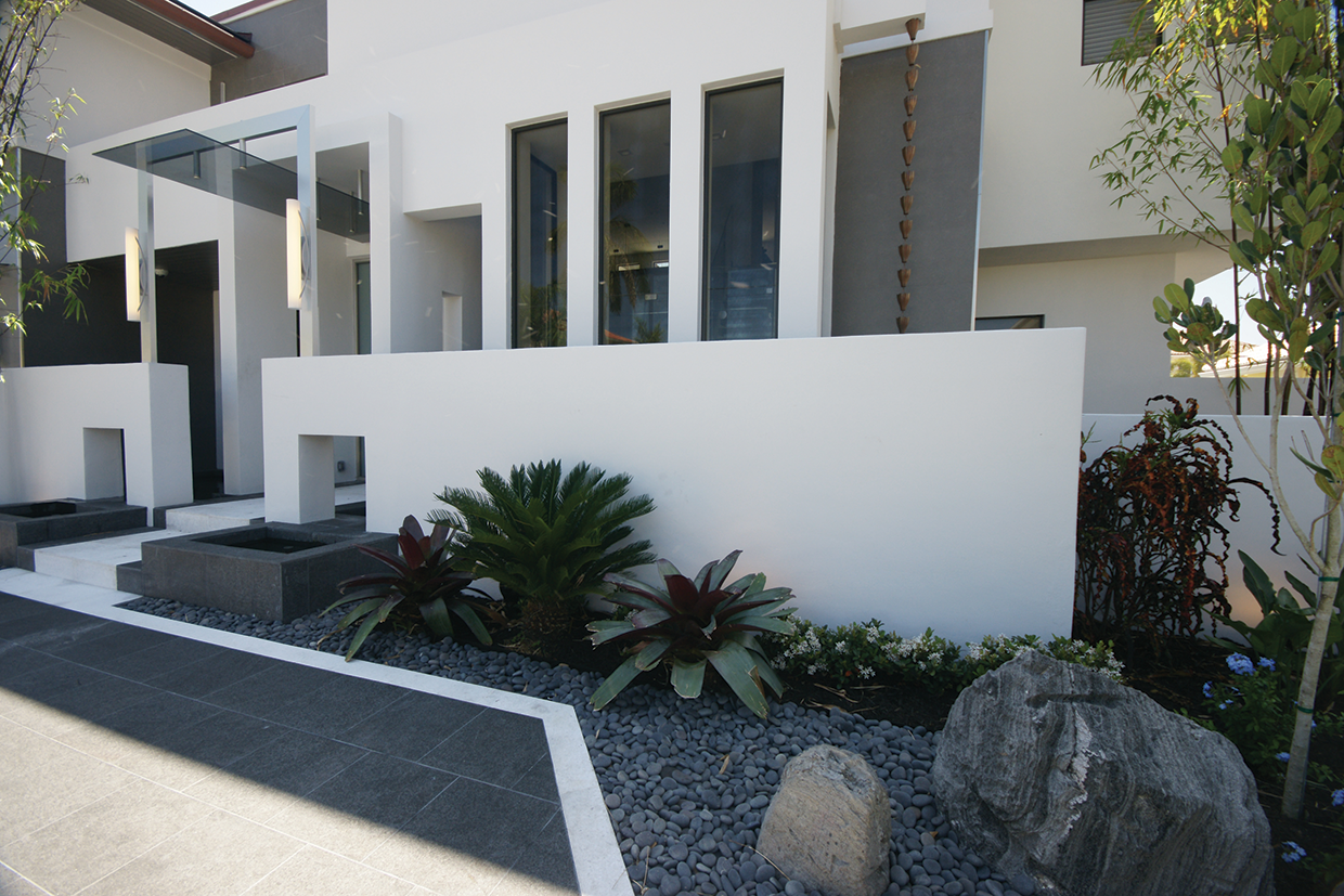 Modern white building illuminated by large outdoor sconce lighting and tasteful rock garden. 