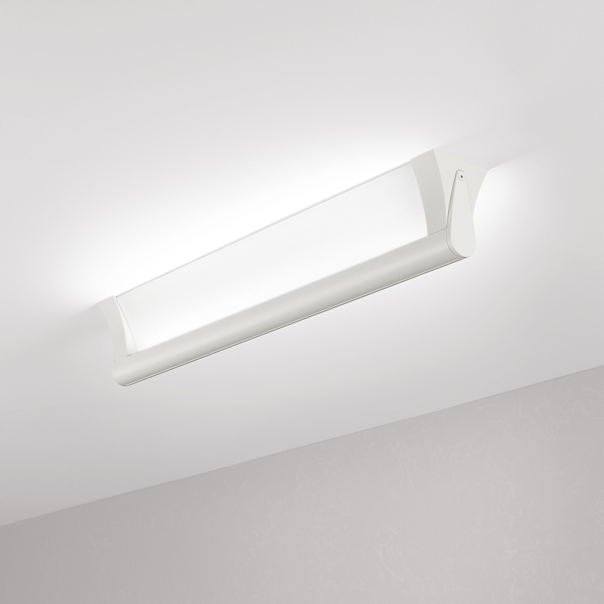 A surface mounted linear luminaire with a body that curves into the base with hidden indirect lighting