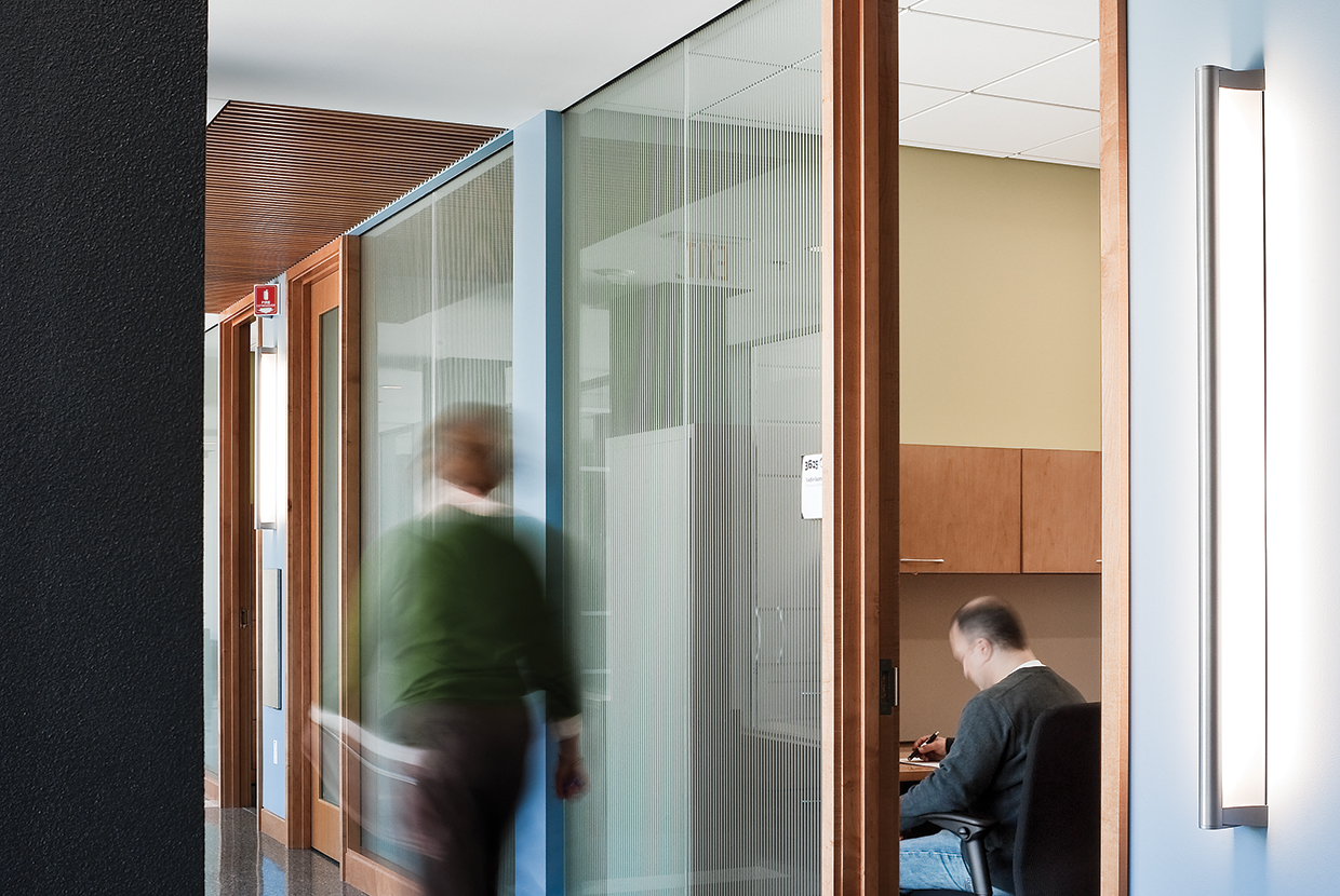 A surface mounted linear luminaire with a body that curves into the base with hidden indirect lighting shown in an office hallway