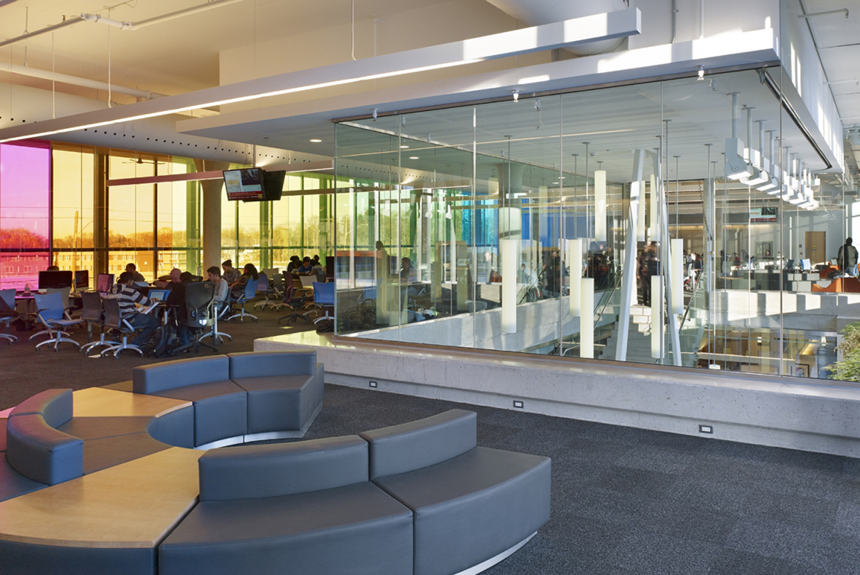 Sequence pendants for education lighting design mounted above a staircase in a large, open campus building lobby. 