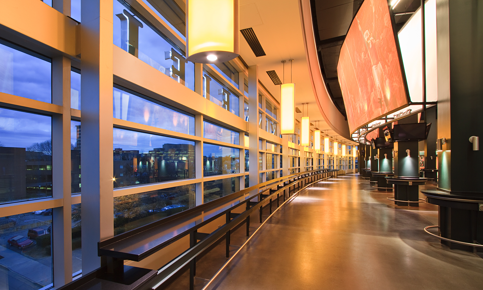 Air Foil education lighting pendants mounted evenly along a curved wall in a college stadium.