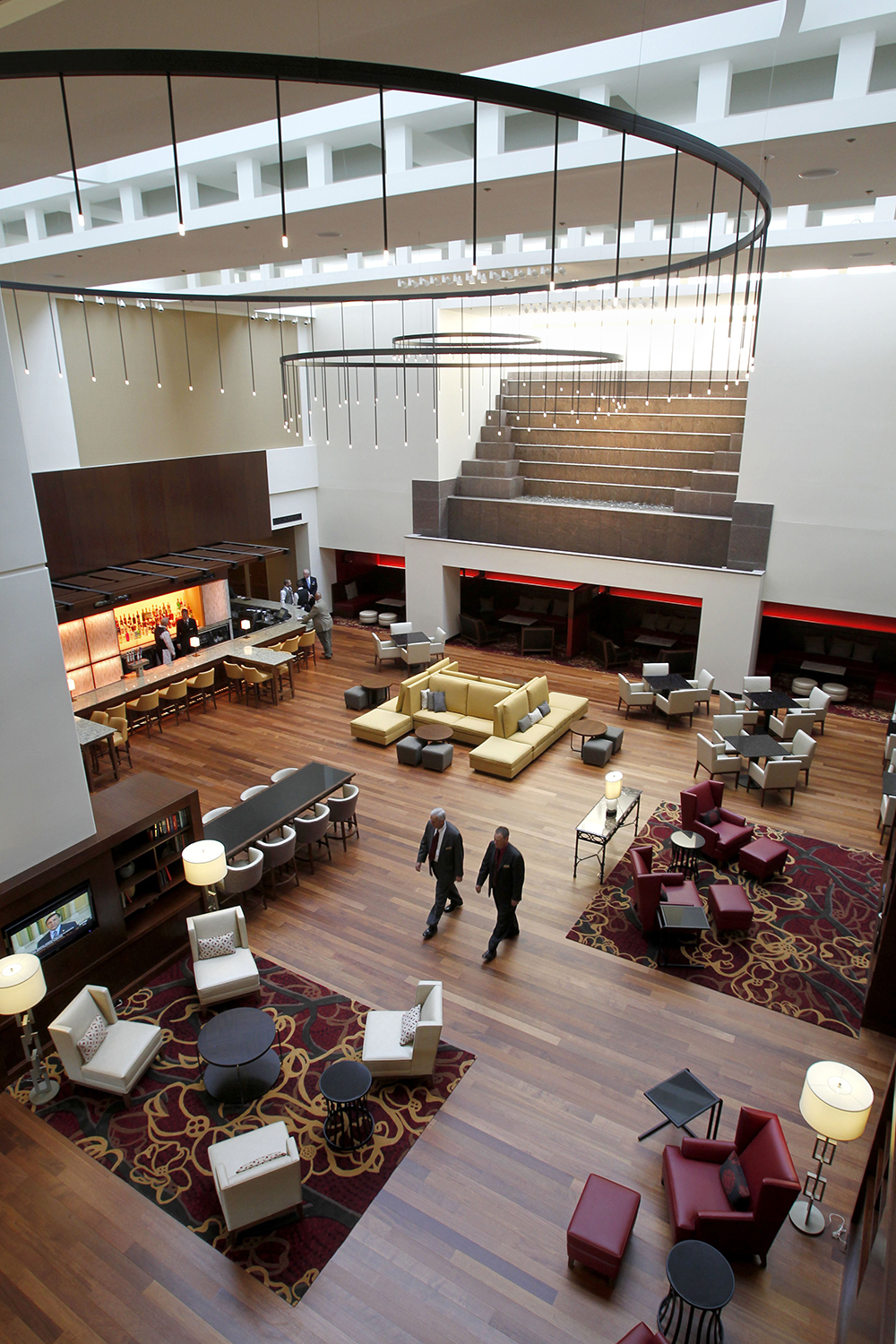 Custom light fixtures circle a stylish hotel lobby with large metal frames and an array of thin downlights.