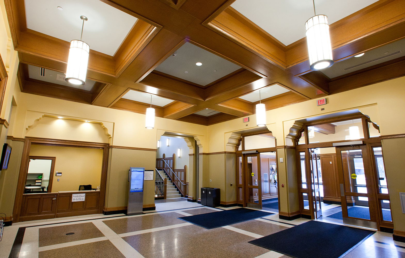 These cylindrical custom light fixtures illuminate a campus entryway with wooden ceiling beams.