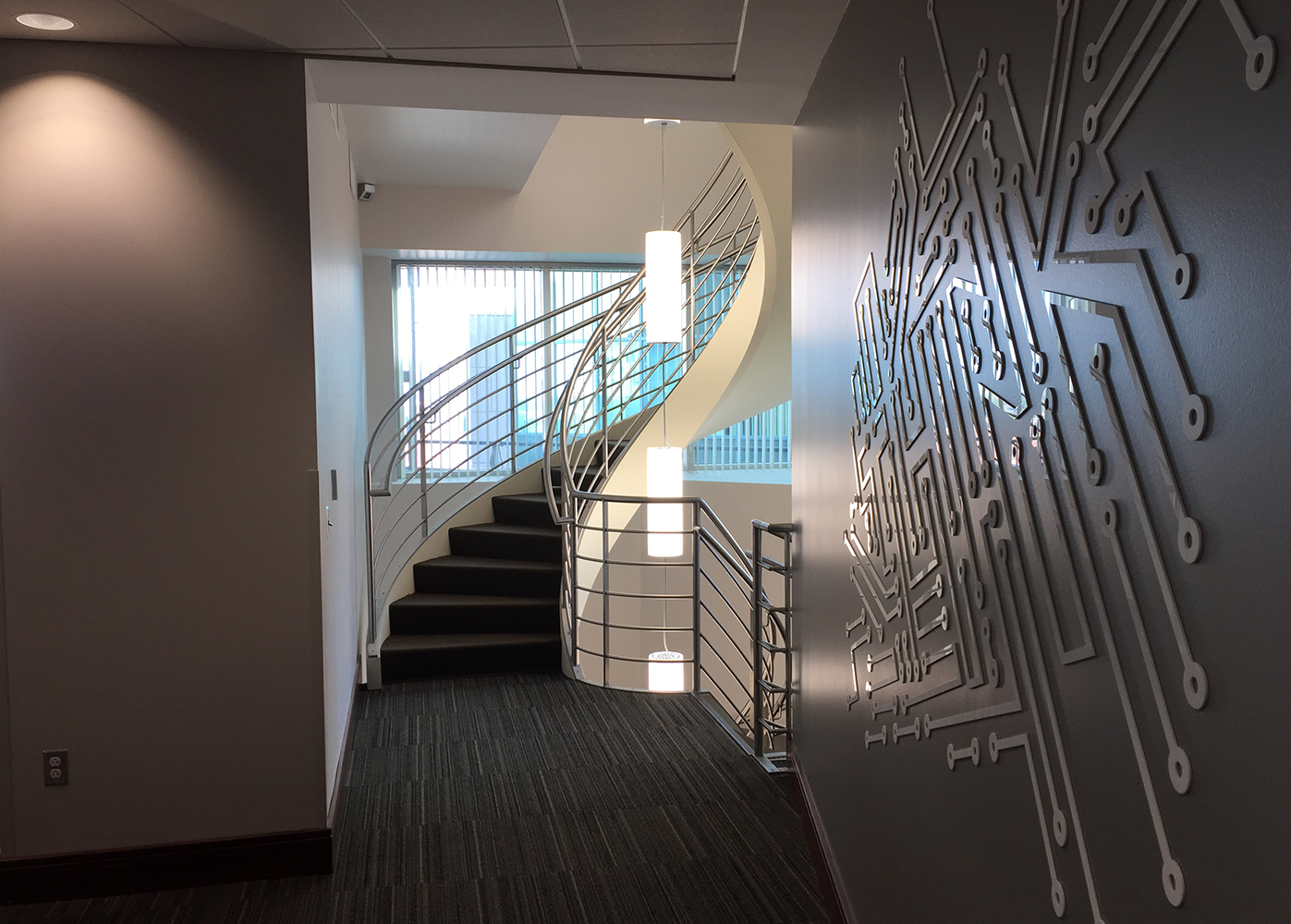 These clean, cylindrical custom light fixtures are hung in tandem down the center of round office stairwell