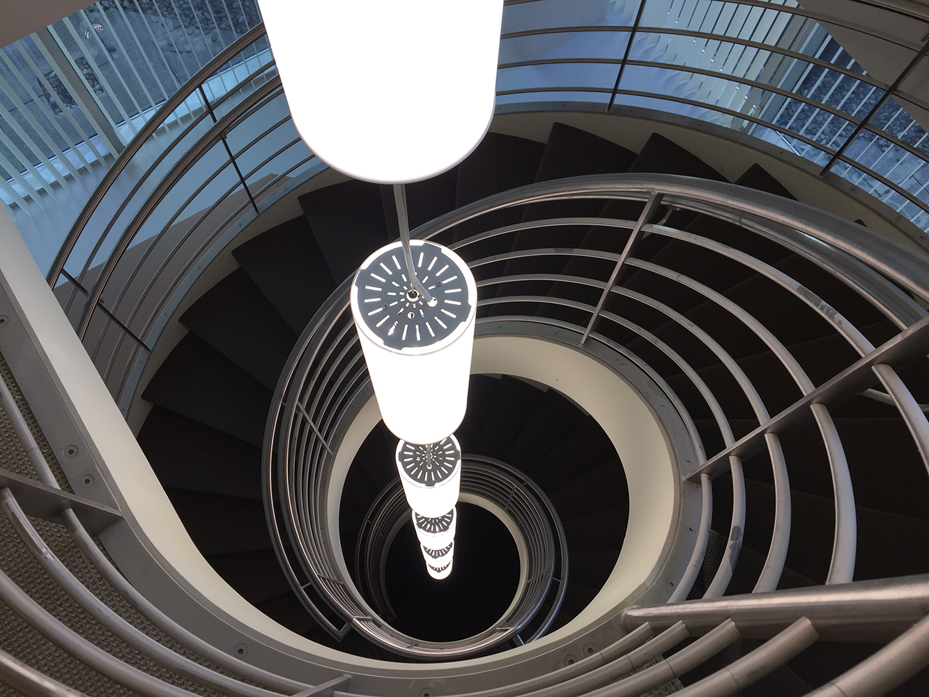 These clean, cylindrical custom light fixtures are hung in tandem down the center of round office stairwell