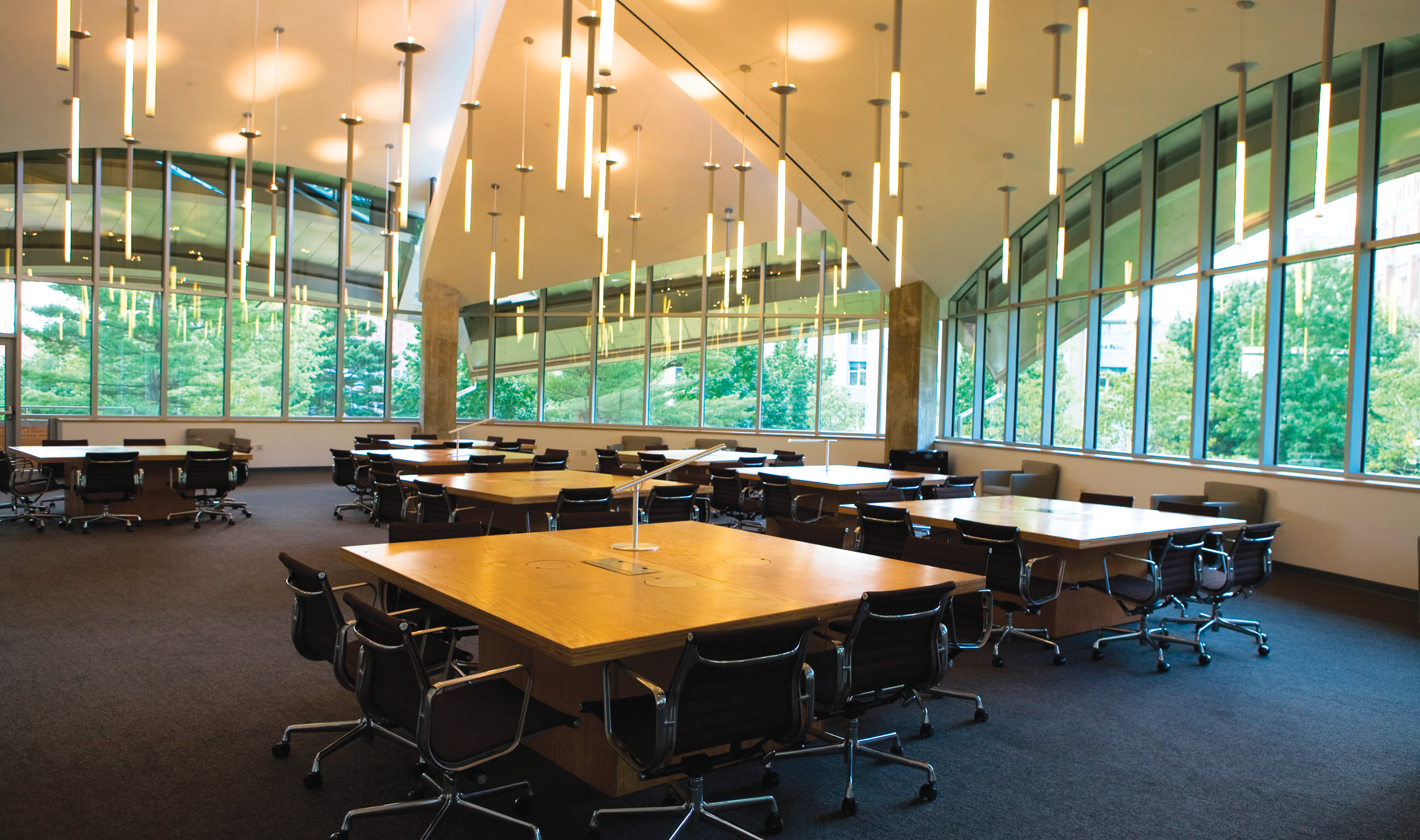 Custom light fixtures in an array of thin luminous tubes brings interest to a large, windowed classroom with group tables.
