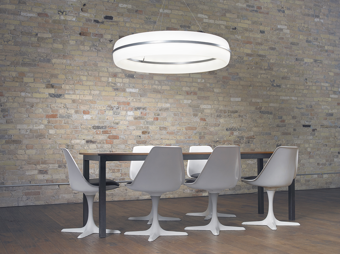 Meridian Round pendant is perfect for office lighting, seen here above a sleek conference table near a brick wall.