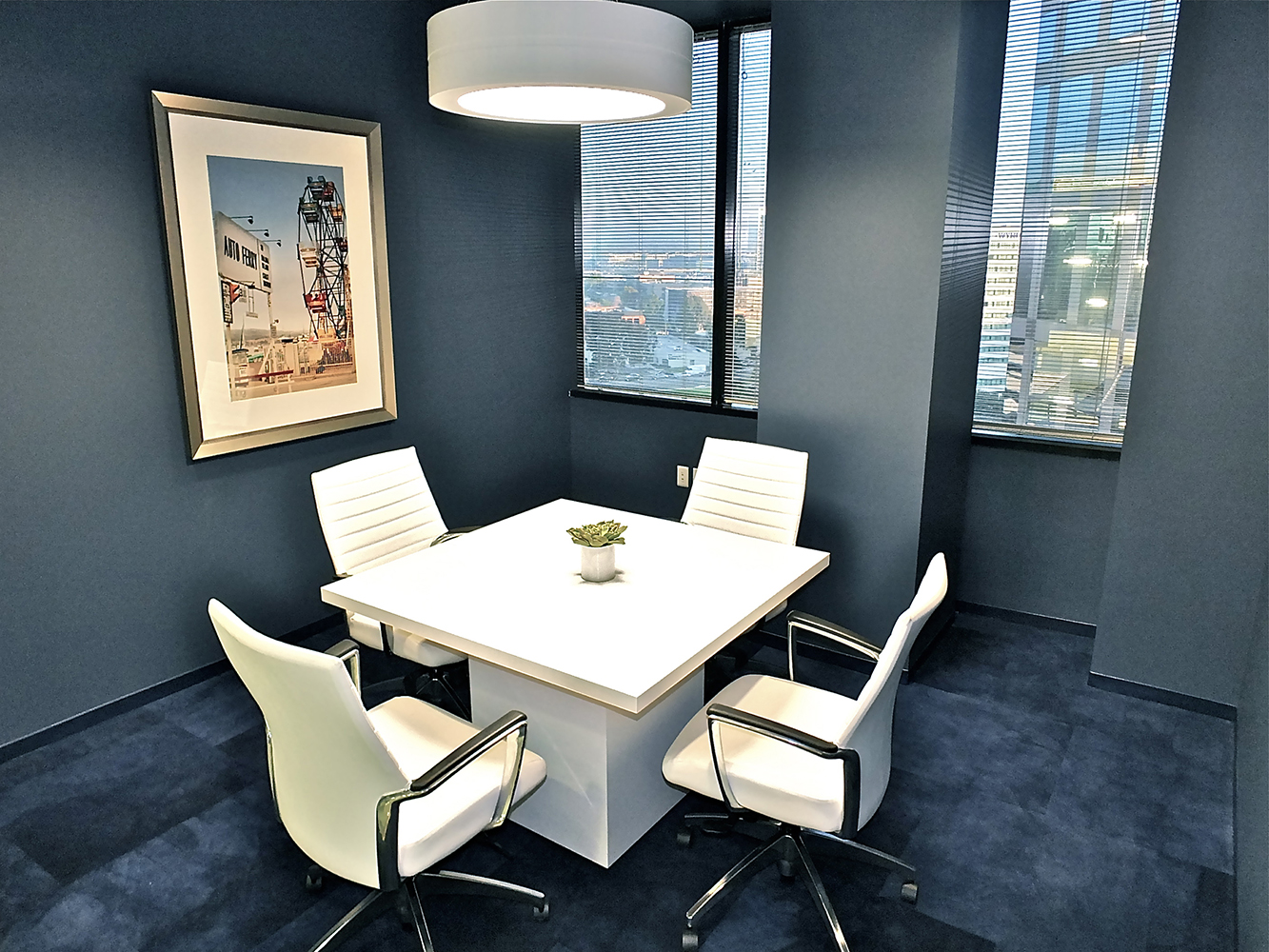 An Omnience pendant in an office lighting application above a small meeting table in a blue-carpeted meeting room.