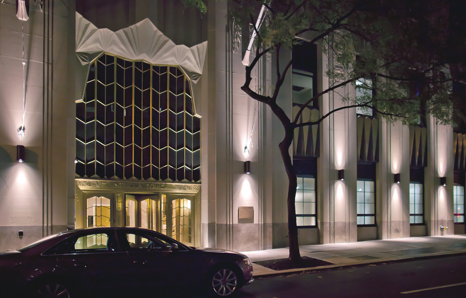 Pla exterior lighting fixtures provide uplight and downlight on a commercial building exterior at night.