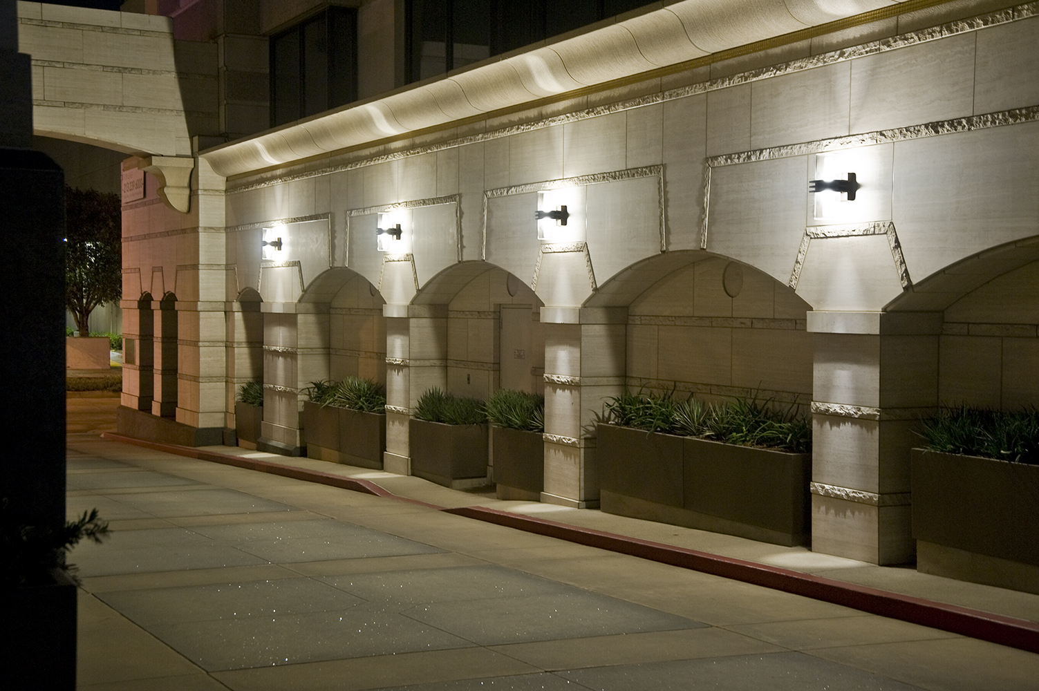 Pla outdoor light fixtures provide uplight and downlight on a classic arch structure along a city street at night.