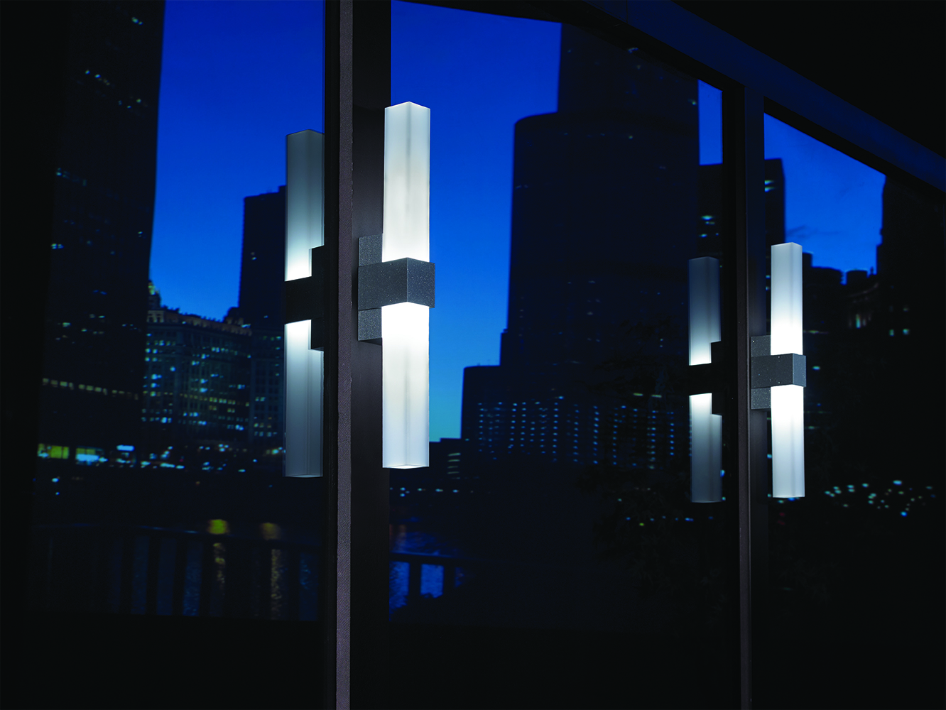 SASS exterior lighting fixtures between large windows at night, reflecting city buildings.