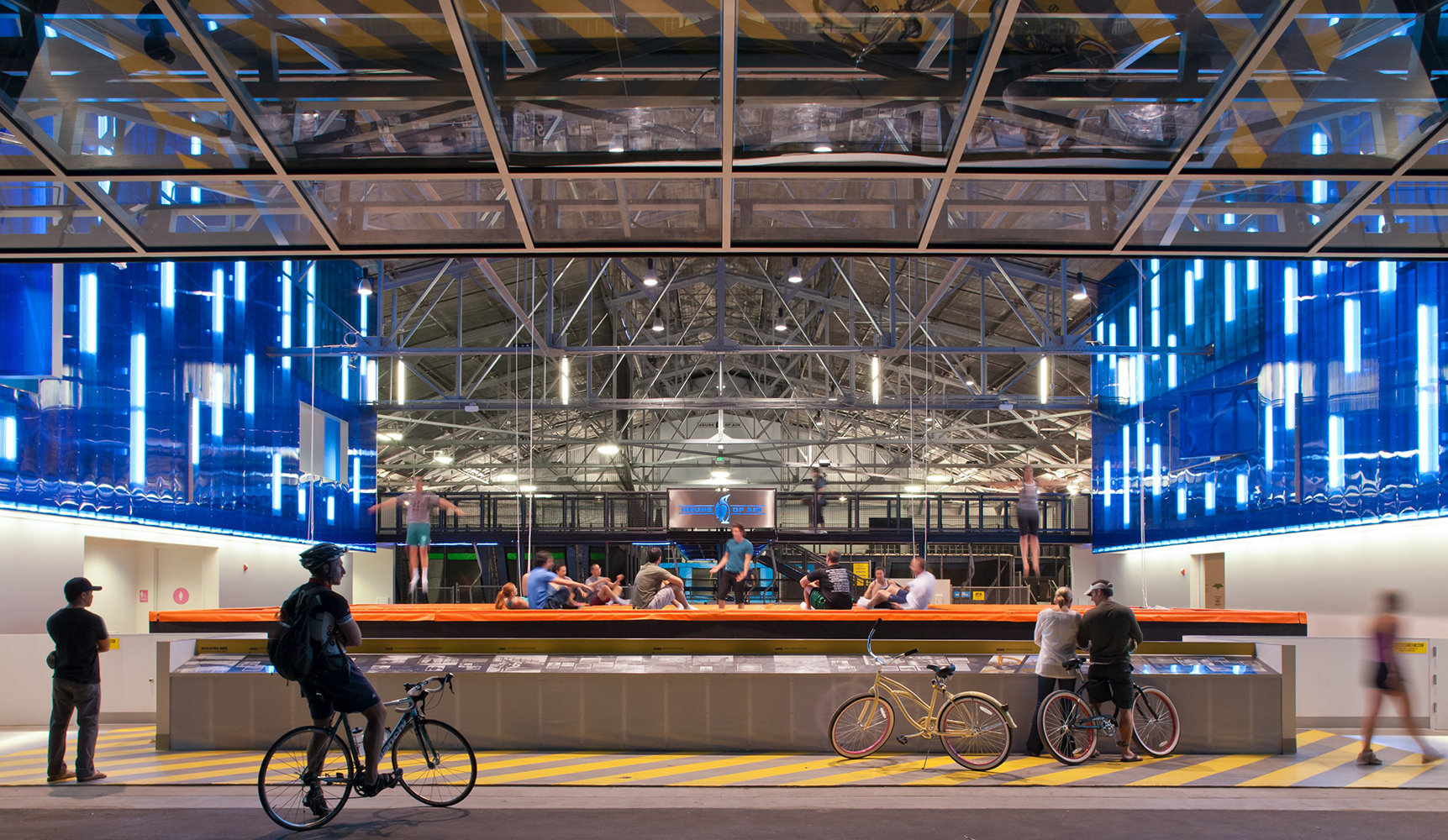 Sequence modern lighting fixtures mounted over a recreational trampoline park, with bicycles in the foreground.