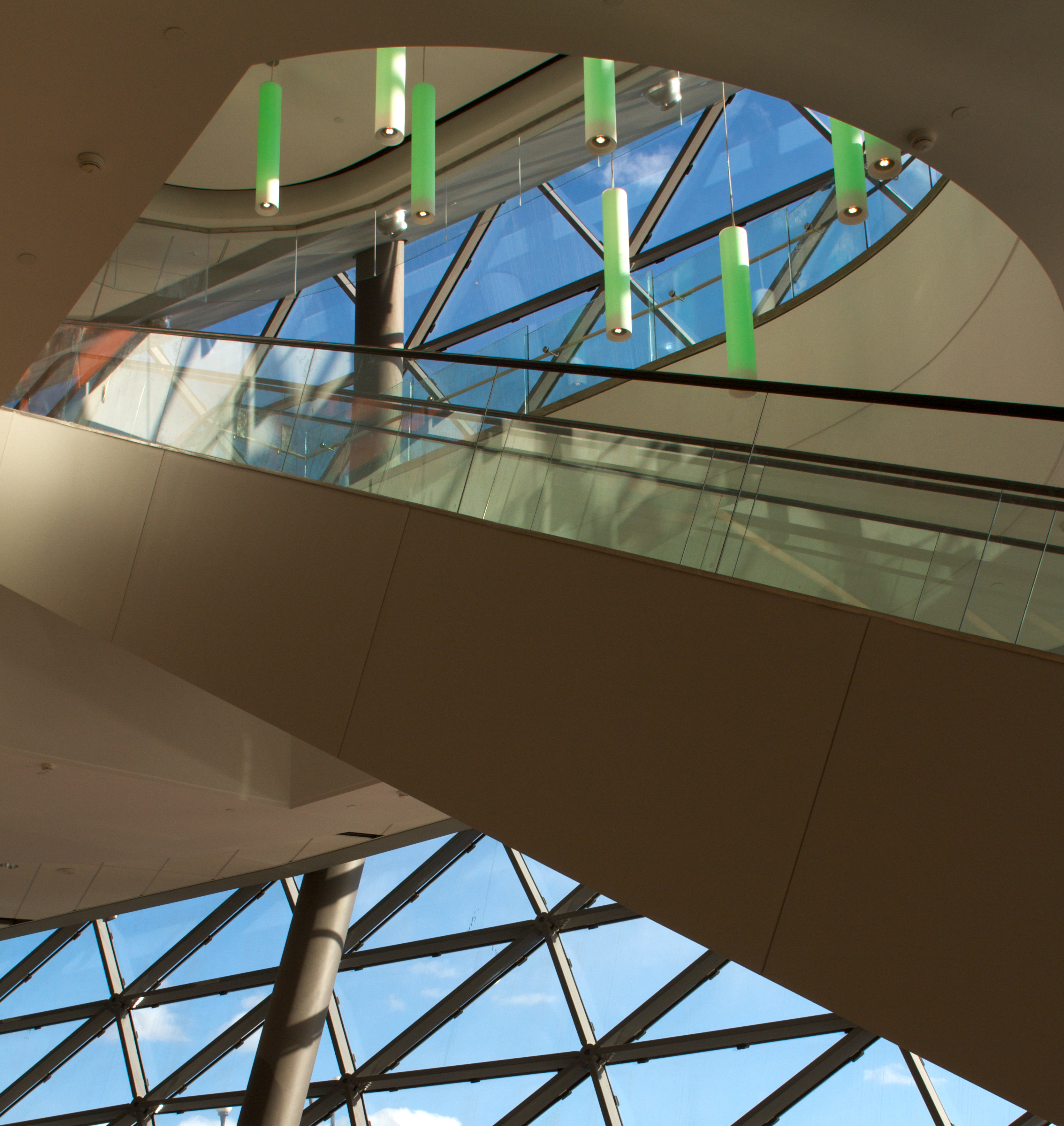 Sequence modern lighting fixtures emit green light over an escalator in a large, well-lit convention center.