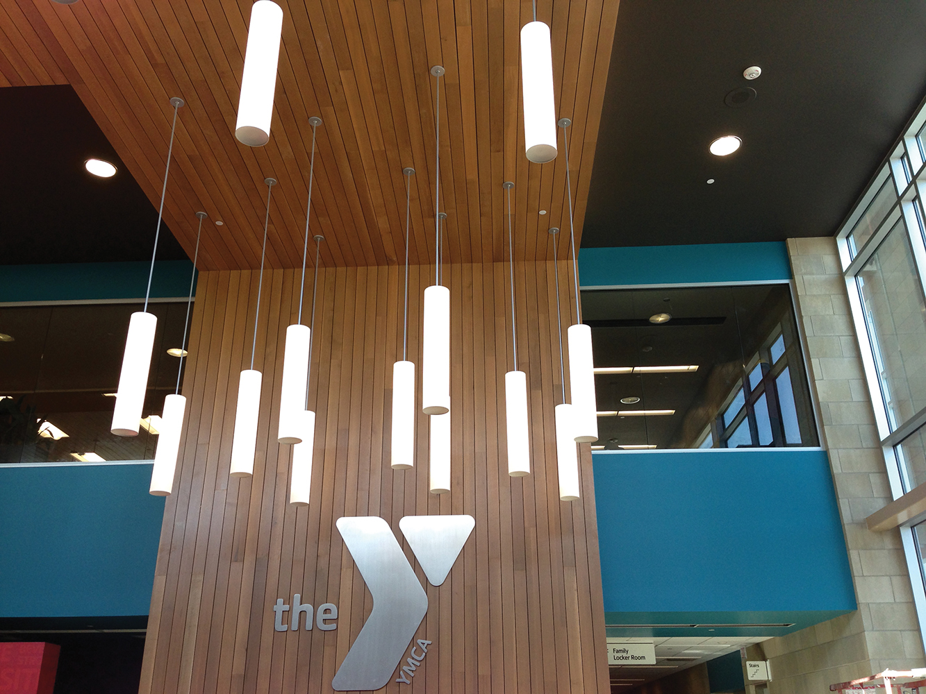 Sequence modern lighting fixtures illuminate a wood-paneled YMCA entryway.