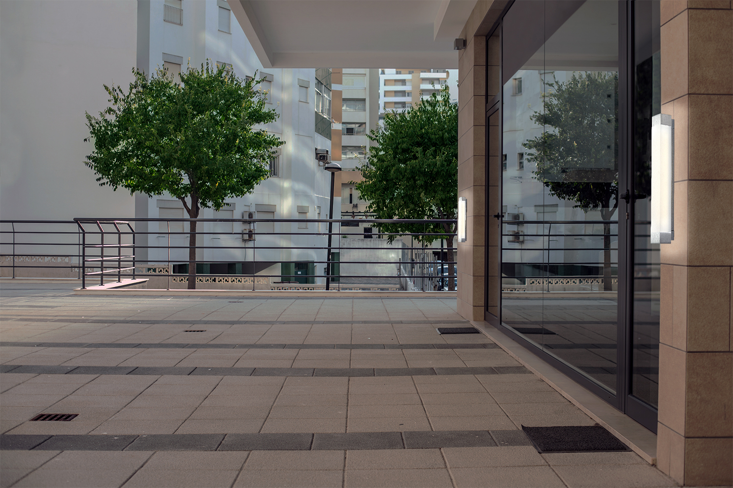 Shine outdoor light fixtures illuminate either side of a large glass door on a metropolitan terrace.