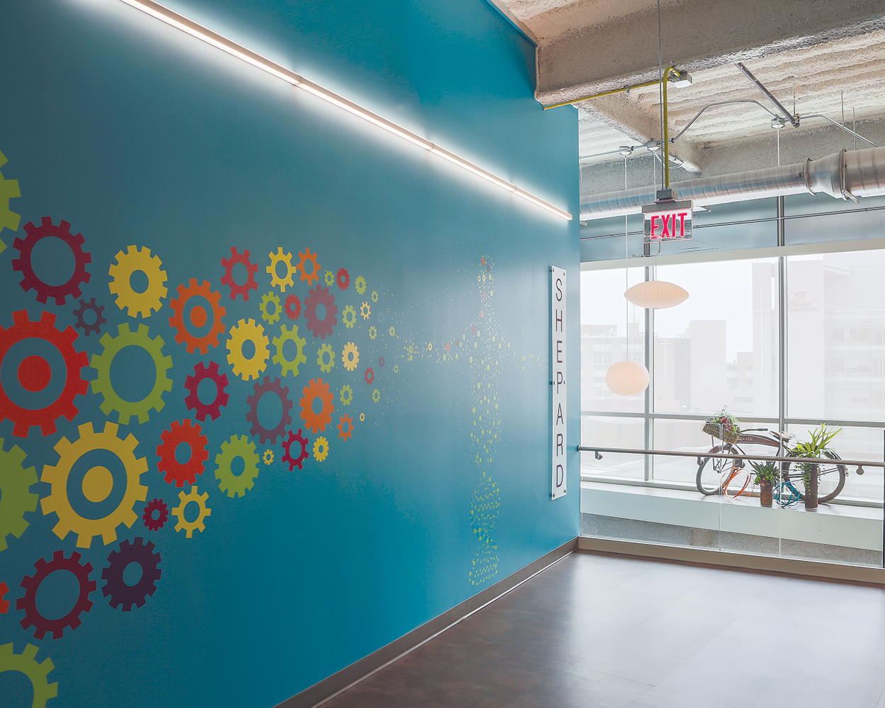 Sleight illuminates a blue wall with colorful gear icons for a modern office lighting design.