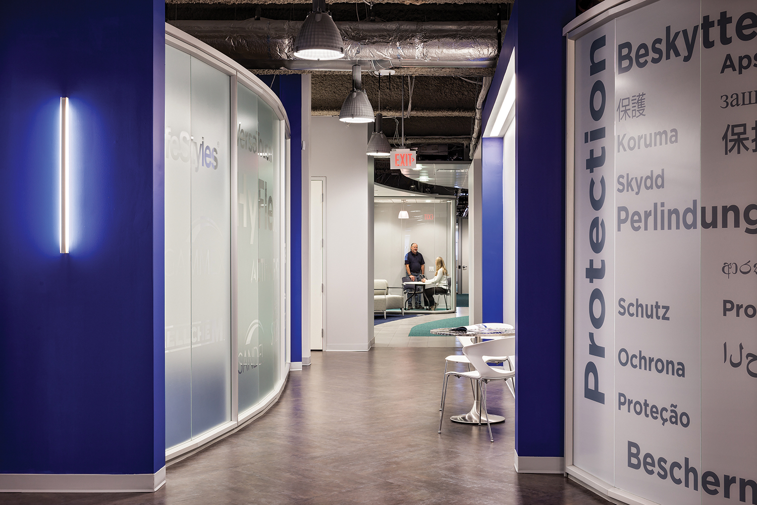 Sleight office lighting fixtures illuminating a blue wall in a workplace corridor with an exposed ceiling.