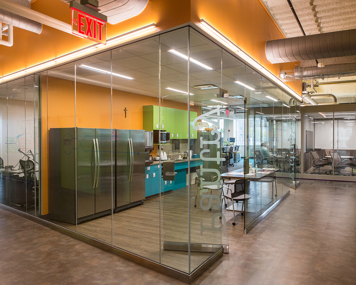 Sleight office lighting fixtures illuminate the edges of a glass-walled workplace kitchen.