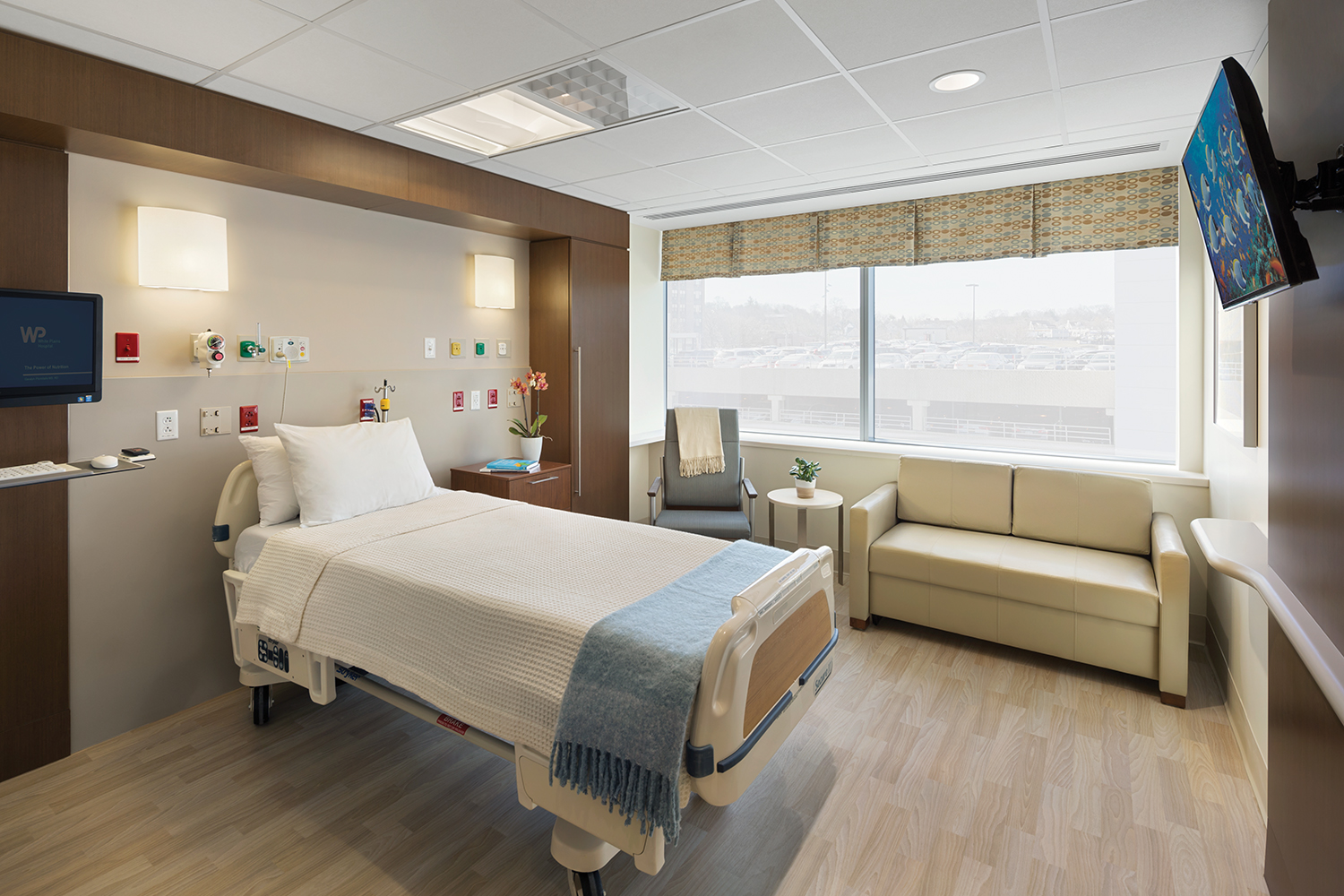 Unity overbed and wall sconce luminaires provide comforting medical lighting in a bright patient room.