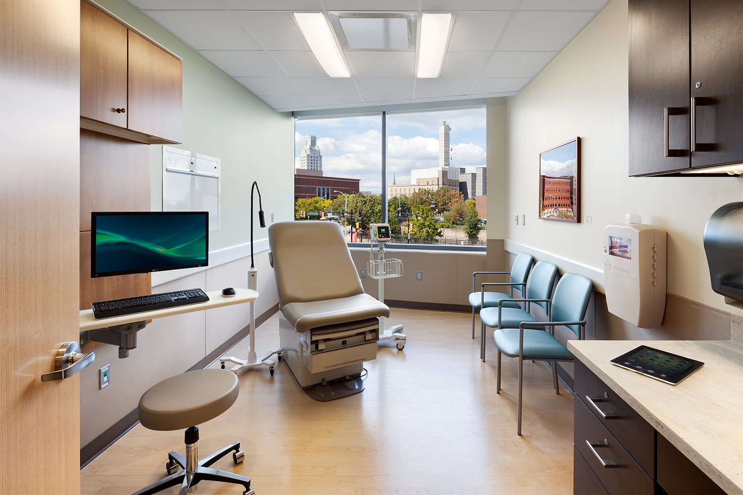Unity tandem ceiling lights in patient room lighting design with an exam chair and medical staff computer.