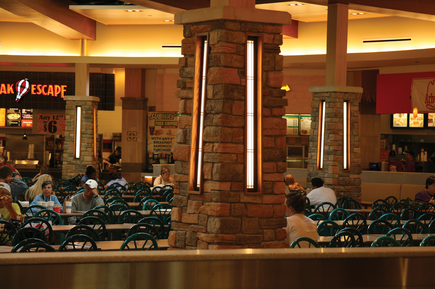 Visage sconces in a stone column provide eye-catching, modern lighting design in a busy mall food court.