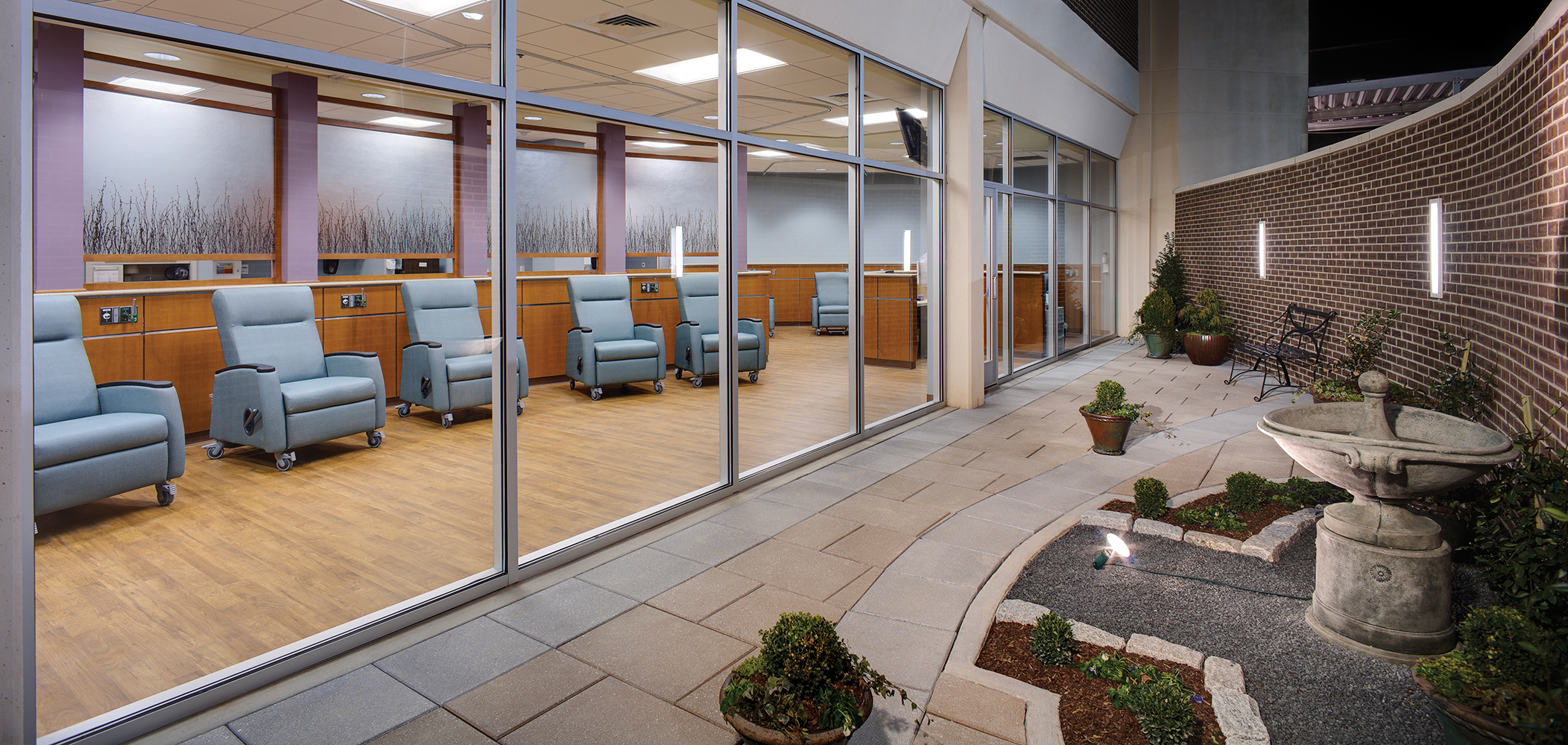 Visage outdoor light fixtures illuminate a medical facility terrace outside a patient seating area.