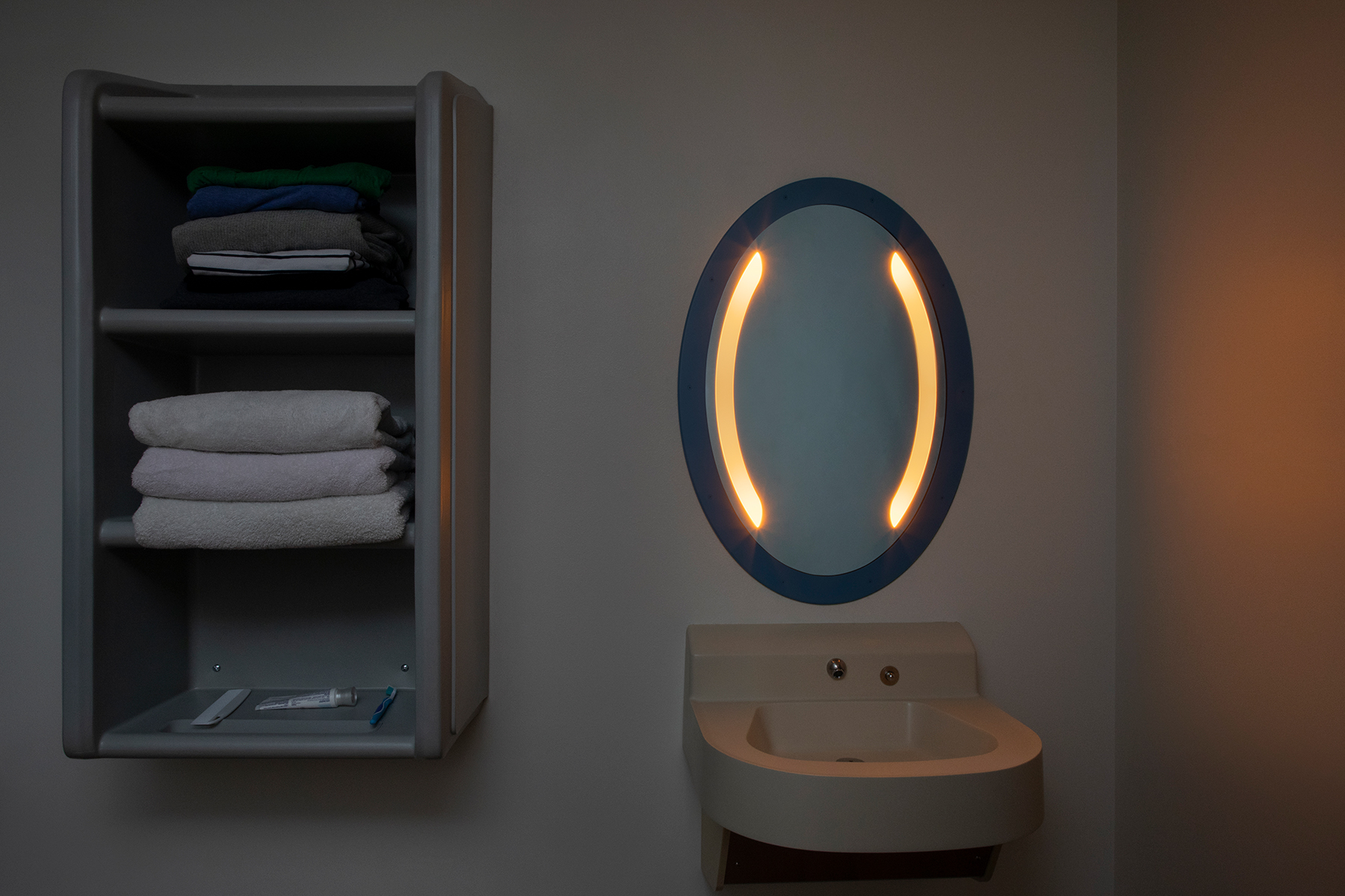 Sole oval illuminated mirror in a behavioral health bathroom with nightlight mode on